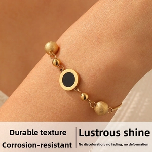Detail of beaded gold chain bracelet showing Roman numeral charm and polished metallic beads