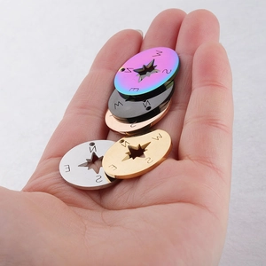 Macro view of 20mm stainless steel compass charms in five metallic finishes on palm