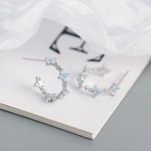 Macro detail of silver S925 C-shaped hoop earrings with light blue four-leaf clover flowers