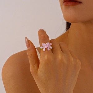Detail of sweet pink resin flower ring featuring green transparent band on female finger