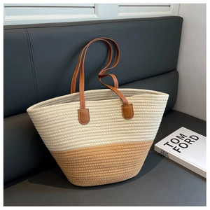 Detail of two-tone woven tote bag with long brown leather handles on a grey bench