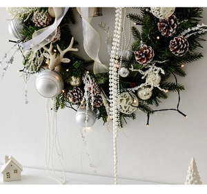 Détails d'une couronne de Noël argentée avec pommes de pin, perles et lumières LED