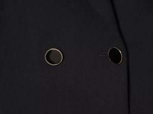 Detail of a black blazer dress featuring black round buttons with gold metallic trim