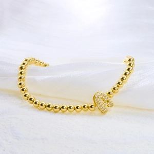 Gold beaded bracelet with sparkling crystal letter A pendant on white silk background