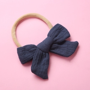 Close-up of baby headband with a navy blue muslin cotton bow on a pink background