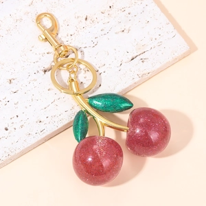 Macro view of sparkly red cherry keychain with green leaves and gold lobster clasp