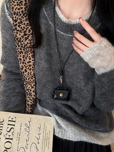 Close-up of a black leather mini neck pouch with snap button on a gray mohair sweater