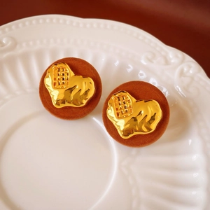 Macro shot of retro gold metal and brown flocked resin earrings on white ceramic
