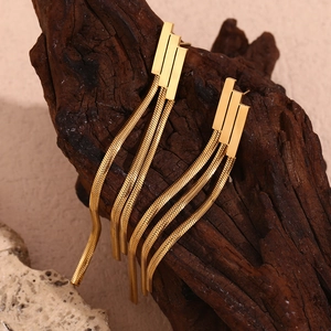 Macro view of 18K gold-plated geometric long fringe earrings on a dark wood background