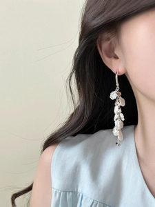 Macro detail of silver tassel earrings with layered metal petals on model