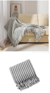 Detail of gray-white striped chunky knit throw blanket with decorative tassels on a sofa