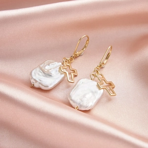 Elegant baroque pearl drop earrings with golden cross charms on pink silk background