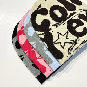Close-up of stacked colorful knit beanies with jacquard graffiti lettering and stars