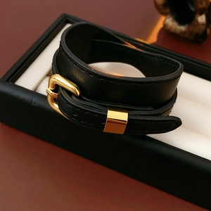 Close-up of black faux leather bracelet with adjustable gold buckle on a display box