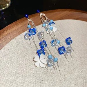 Elegant blue acrylic flower tassel earrings with silver chains on a rustic linen background