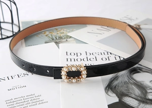 Detail of black patent leather belt with pearl-embellished square buckle on white table