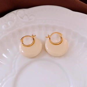 Detail view of 18k gold plated round resin earrings placed on white relief porcelain plate