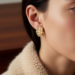 Close-up of 14k gold plated wave earrings with pearl clusters on a model wearing knitwear