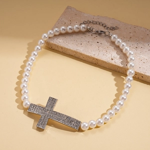 Detail of beaded necklace with large rhinestone cross pendant on stone surface