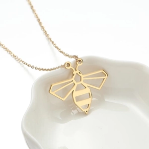 Minimalist gold hollow honey bee pendant necklace on a decorative white porcelain dish