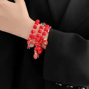 Détail du bracelet multi-rangs en perles rouges avec breloque chat porte-bonheur dorée