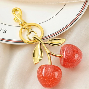 Close-up of a glittery red cherry keychain with gold metal chain on a white ceramic plate