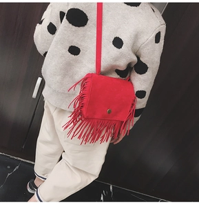 Detail of red suede kid's crossbody bag featuring decorative tassels and smooth texture