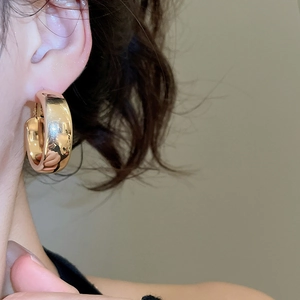 Close-up of a wide gold C-shaped earring with a polished metallic finish on a model