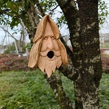 Detailed view of hand-carved wooden birdhouse in elderly man shape on a tree trunk
