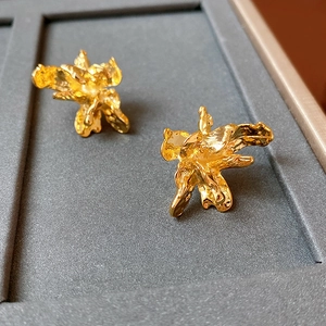 Dettaglio di orecchini vintage in metallo dorato a forma di fiore su vassoio grigio