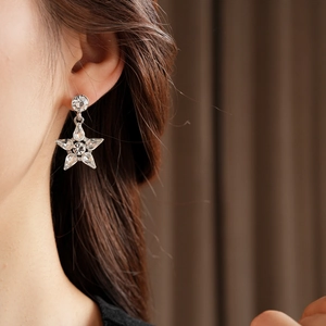 Detailed close-up of a silver star-shaped earring with crystals on a female model
