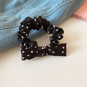 Detailed view of a black and white polka dot bow scrunchie on blue denim fabric
