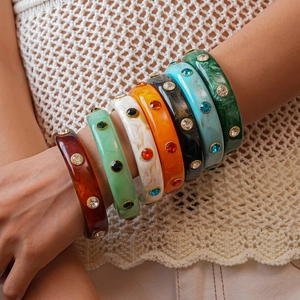 Close-up of stacked colorful acrylic resin bangles with embedded rhinestones on model arm