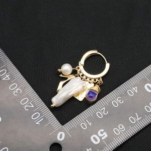 Elegant gold pearl earrings with purple gemstone and handmade tag on black background