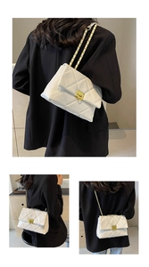Detail view of white quilted crossbody bag featuring gold chain strap and square lock buckle