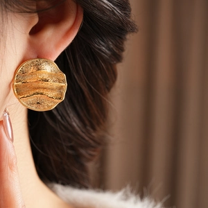 Détail de boucles d'oreilles dorées avec texture ondulée sur un modèle élégant