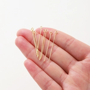 Hand holding 18K gold-plated eye pins for DIY jewelry making on white background