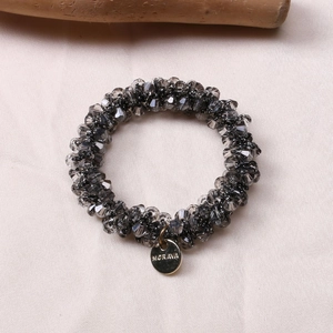 Detailed view of faceted grey crystal beads and golden metallic logo charm on silk