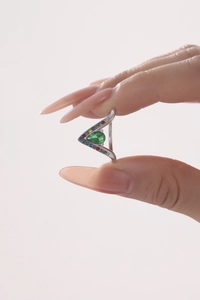 Vue macro d'une bague en V avec pierre verte et diamants colorés sur les côtés