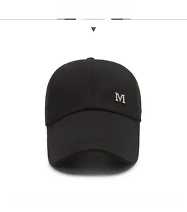 Close-up of a minimalist black baseball cap featuring a silver metal M logo on the brim
