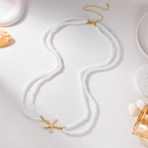Detail of layered pearl body chain featuring a gold starfish charm and shell accents