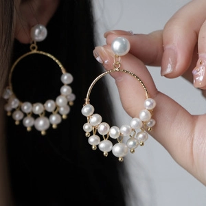 Detail view of large gold hoop earrings adorned with lustrous white baroque pearls