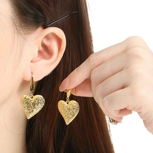 Close-up of heart-shaped gold earrings with a hammered metal texture worn by a model