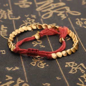 Detalle de la pulsera trenzada roja con cuentas doradas y elegantes borlas