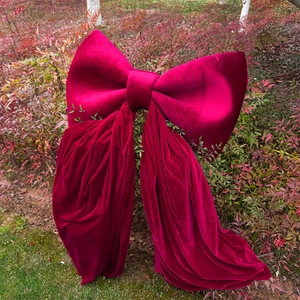 Giant dark red velvet bow ornament displayed outdoors on a natural bush background