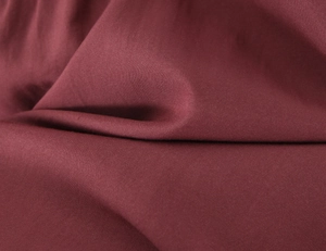 Macro shot of burgundy textile fabric showing fine woven texture and soft pleats
