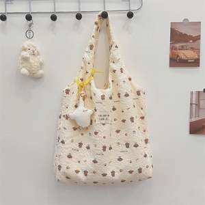 Close-up of beige quilted tote bag with brown bear prints and a plush goose charm