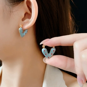 Detailed close-up of a blue heart earring with red polka dots and a golden hinge clasp