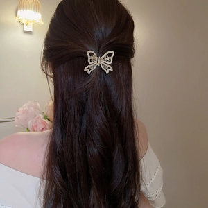 Detail of a hollow golden butterfly hair claw with pearls on dark brown hair