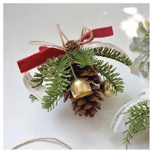 Detailed view of Christmas pinecone ornament with green needles, red bow and gold bell
